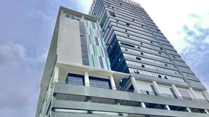 Een hoog gebouw met een modern architectonisch ontwerp, meerdere balkons en een opvallend 'OZOO'-bord.