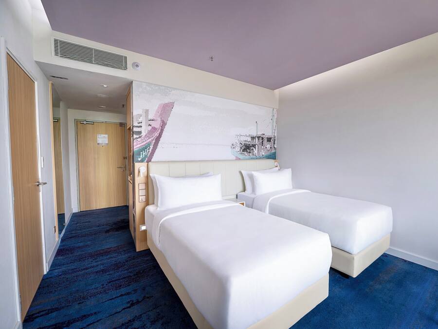 A hotel room with two beds, a large painting on the wall, a blue carpet, and a small table.