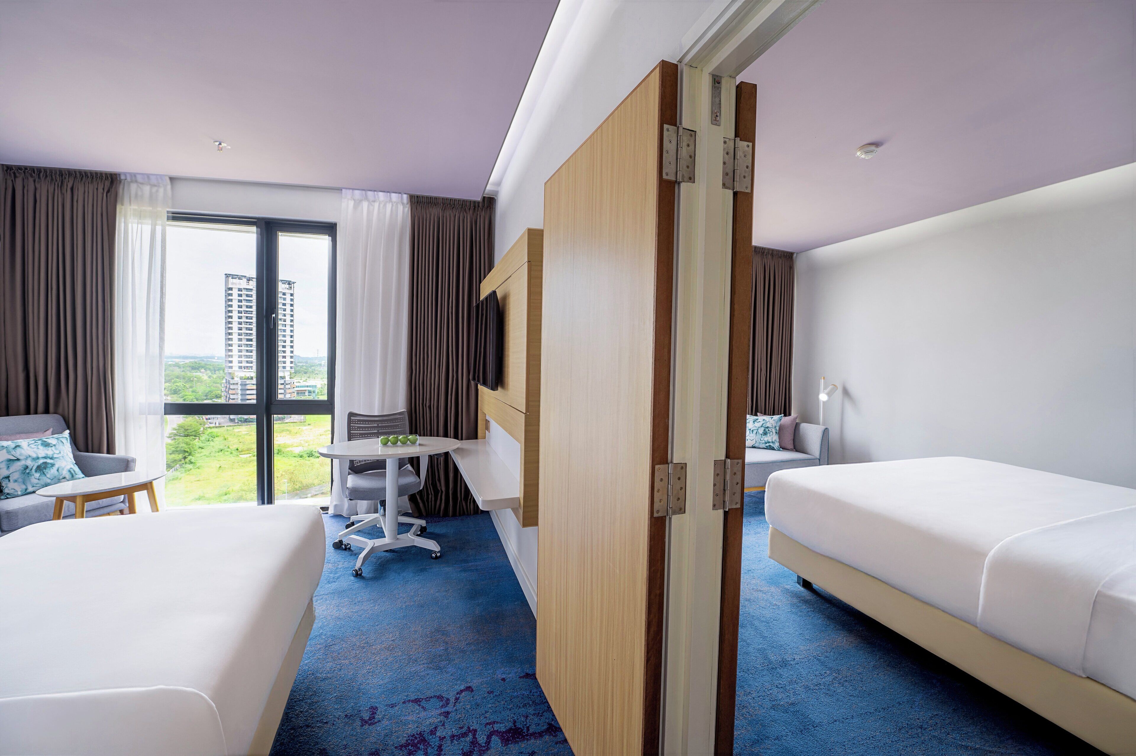 A hotel room with two beds, a desk, and a view of a cityscape.