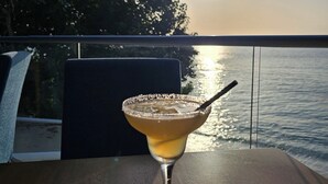 A cocktail on a table with a view of the ocean and trees in the background.