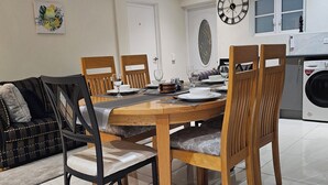A dining area with a wooden table and chairs, a sofa, and a washing machine in the background.