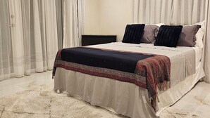 A bedroom with a bed, a nightstand, a ceiling fan, and sheer curtains.