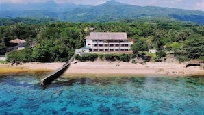 Un hotel costero con vista a la playa, rodeado de exuberante vegetación y montañas al fondo.
