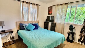 Un dormitorio con cama, escritorio, silla, ventilador y ventana con cortinas.