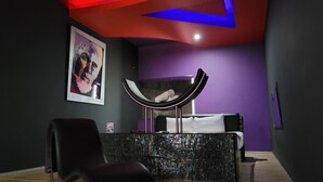 A modern bedroom with a black and white bed, a hammock chair, and a colorful abstract painting on the wall.