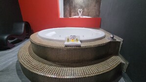 A bathroom with a large, circular, mosaic-tiled bathtub, a towel rack, and a small towel with a duck design.