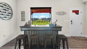 Une cuisine avec un coin bar, des tabourets, un meuble à vin et une vue sur un champ par la fenêtre.