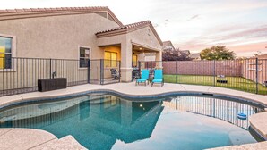 A swimming pool with a curved edge, a covered patio area with chairs, and a fenced backyard. - Tucson pool home -  pets, putting green, no hidden fees (Tucson)