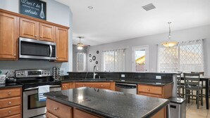 A modern kitchen with wooden cabinets, a stainless steel microwave, a built-in oven, and a granite countertop. - Tucson pool home -  pets, putting green, no hidden fees (Tucson)