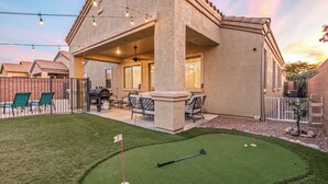 A house with a patio, outdoor seating, and a small lawn with a golf hole. - Tucson pool home -  pets, putting green, no hidden fees (Tucson)