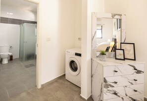 A modern bathroom with a washing machine, a toilet, and a marble vanity with a mirror.