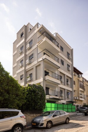 Un immeuble résidentiel à plusieurs étages, doté de balcons, de climatiseurs et d’une barrière de protection verte.