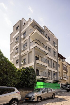 A multi-story residential building with balconies, air conditioning units, and a green construction barrier.