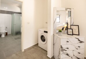 Une salle de bain moderne équipée d’un lave-linge, de toilettes et d’une douche à parois de verre.