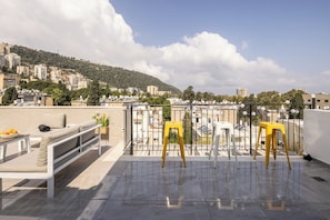 A rooftop terrace with a white sofa, yellow stools, and a table with fruits.