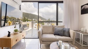 Una sala de estar moderna con un sofá, una mesa de centro y vistas de un paisaje urbano a través de amplios ventanales.