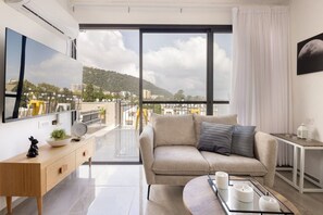 A modern living room with a sofa, a coffee table, and a view of a cityscape through large windows.
