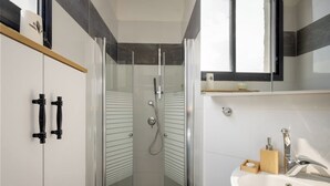 Un baño moderno con cabina de ducha de vidrio, un lavabo blanco y un espejo sobre el lavabo.