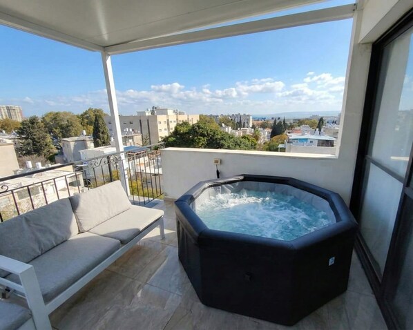 A balcony with a hot tub, a sofa, and a view of the cityscape.