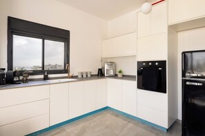 A modern kitchen with a large window, a black refrigerator, and a coffee maker.