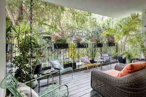 Een terras buiten met rieten meubels, potplanten en uitzicht op het omliggende groen.