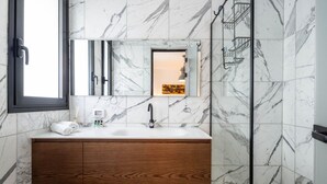 A bathroom with a marble wall, a wooden vanity, a white sink, and a glass shower enclosure. - Mamad Stylish Green Oasis | Tel Aviv Old North (Tel Aviv)