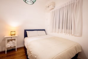 Een slaapkamer met een bed, een nachtkastje met een lamp en een raam met gordijnen.