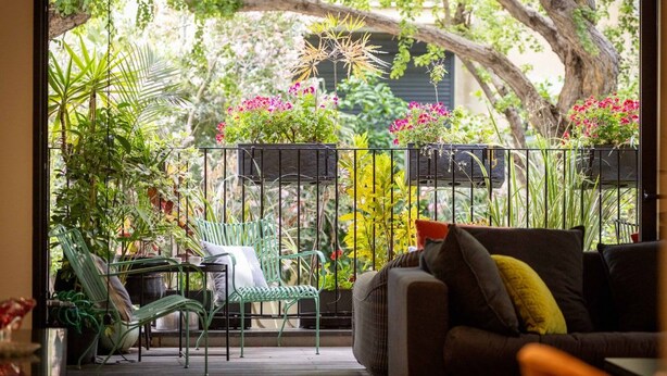 A balcony with a sofa and chairs, surrounded by potted plants and flowers. - Mamad Stylish Green Oasis | Tel Aviv Old North (Tel Aviv)