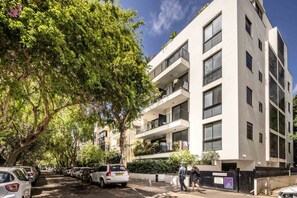 Un edificio residencial de varios pisos con balcones, coches aparcados y árboles.