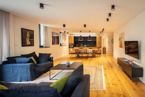 Een moderne woonkamer met een bank, salontafel en een eethoek op de achtergrond.