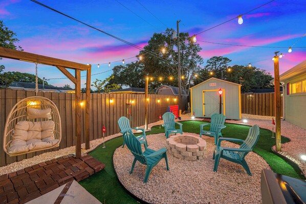 Un patio trasero con cerco de madera, una silla colgante, un brasero y mobiliario exterior.
