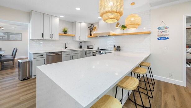 Une cuisine moderne avec des meubles blancs, un grand îlot central et des luminaires suspendus.