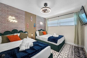 Una habitación de hotel con dos camas, una pared de ladrillo, un letrero de neón, un ventilador de techo y un televisor.