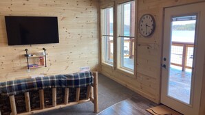 Une pièce aux murs en bois, avec un banc, une horloge murale et une porte donnant sur l’extérieur.