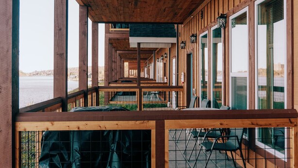 Une terrasse en bois offrant une vue sur un plan d’eau, avec une rangée de fenêtres et des sièges d’extérieur.
