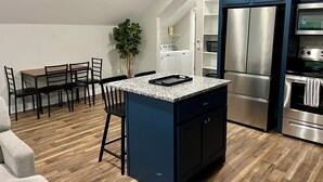 Een moderne keuken met een centraal eiland, inbouwapparatuur en een eethoek met stoelen.