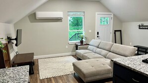 Een moderne woonkamer met een hoekbank, een flatscreen televisie aan de wand, een raam met uitzicht op groen en een deur met een raam.
