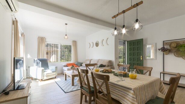 Comedor con mesa dispuesta para seis, sillas de madera, mantel a rayas y una jarra de jugo de naranja.