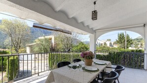 Un espacio de comedor al aire libre cubierto, con una mesa preparada para dos personas, sillas alrededor y vistas del paisaje.