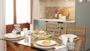 Una mesa de comedor dispuesta con platos, croissants y tazas de café, con una cocina al fondo.