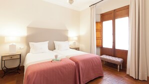 Habitación de hotel con una cama grande, dos mesitas de noche, un banco y una ventana con cortinas.