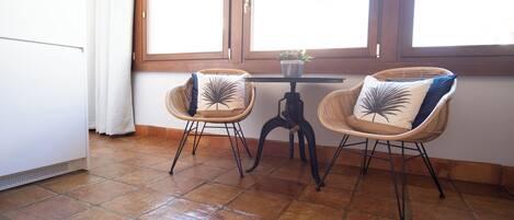 A room with two wicker chairs, a small table with a plant, and a window with curtains.