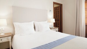 A neatly made bed with white linens and a blue accent, a wooden nightstand with a lamp, a wooden wardrobe, and a door with a mirror. - El Envero en La Casa del Aceite (Cordoba)