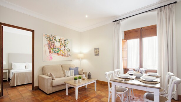 A well-lit room with a sofa, a dining table set for four, and a painting on the wall. - El Envero en La Casa del Aceite (Cordoba)