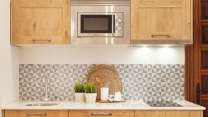 A kitchen with wooden cabinets, a stainless steel microwave, a sink, and a backsplash with a geometric pattern. - El Envero en La Casa del Aceite (Cordoba)