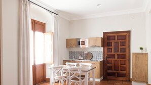 A kitchen with white cabinets, a wooden door, and a dining area with white chairs and a table. - El Envero en La Casa del Aceite (Cordoba)