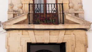Un edificio de piedra con un balcón que tiene barandillas de hierro forjado y una puerta de madera con un ventanal arriba.