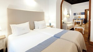 Habitación de hotel con dos camas, una zona de estar y vista a la cocina.