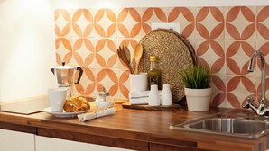A kitchen counter with a coffee maker, croissant, salt and pepper shakers, a bottle of olive oil, a woven basket, and a potted plant.