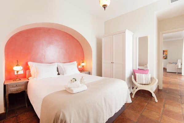 Habitación de hotel con una cama grande, un armario, una tocador con espejo y una pequeña zona de estar.
